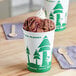 A cup of ice cream with chocolate, sprinkles, and a tree design on the cup.