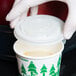 A hand in a glove holding a EcoChoice compostable plastic lid over a white cup.