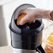 A person's hand squeezing an orange into an AvaMix electric citrus juicer.