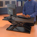 A man standing at a Luxor adjustable standing desk with a computer.