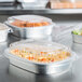 A Durable Packaging aluminum foil take-out container filled with a variety of food on a table.