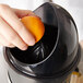 A hand holding an orange squeezing it into a black juicer with a white splash guard.