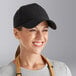 A woman wearing a black Choice 6-panel cap in a professional kitchen.