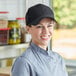A woman in a chef's uniform smiling and wearing a black Choice 6-panel cap.