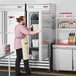 A man opening an Avantco stainless steel solid door reach-in freezer in a professional kitchen.