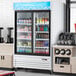 An Avantco white sliding glass door merchandiser refrigerator with drinks and beverages on display.