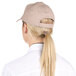 A woman with a ponytail wearing a beige Choice khaki 6-panel cap.