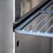 A metal shelf on a metal surface inside an Avantco stainless steel reach-in refrigerator.