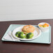 A sky blue Cambro tray with a sandwich, broccoli, and a plate of fruit.