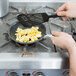 Scrambled eggs cooking in a Vollrath stainless steel non-stick fry pan on a stove top.
