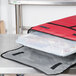 A red and black Intedge insulated food carrier with a plastic container inside.