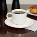 A white Arcoroc porcelain cup of coffee on a table with a white porcelain saucer holding a pastry.