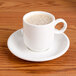 An Arcoroc white porcelain cup with a foamy drink on a saucer.
