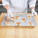 A chef using a Chicago Metallic wire in rim aluminum sheet pan to bake cinnamon rolls.