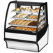 A True curved glass white dry bakery display case full of pastries.