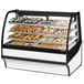 A True curved glass white dry bakery display case on a counter with trays of pastries.