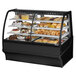 A True 59 1/4" Curved Glass Black Dual Service Refrigerated Bakery Display Case displaying various pastries.