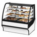 A True dual service refrigerated bakery display case with curved glass on a counter with various baked goods inside.