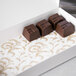 A white 7 3/8" x 3 7/8" glassine pad with gold floral pattern holding three chocolate bars.