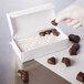 A hand holding a 1-Piece white candy box filled with chocolates.