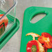 A green Rubbermaid cutting board with tomatoes on it.