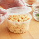 A gloved hand holding a ChoiceHD translucent plastic deli container of macaroni and cheese with the lid open.