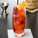 A Reserve by Libbey highball glass filled with red liquid, a straw, and garnished with orange slices and cherries.