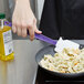 A person using a Rubbermaid purple high temperature spatula to stir pasta in a pan.