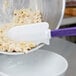 A purple and white Rubbermaid high temperature silicone spatula mixing noodles.