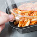 A hand holding a Solut clear plastic lid on a plastic container of pasta.