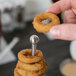 A hand holding a Clipper Mill stainless steel tower with fried onion rings stacked on it.