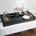 A chef cooking food on a Tablecraft black brushed aluminum countertop induction station.