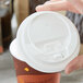 A person's hand holding a white Choice paper cup with a hinged white plastic lid.
