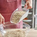 A woman using a Choice clear plastic utility scoop to pour oats into a bowl.