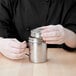 A woman's hands using a Vollrath stainless steel shaker/dredge with handle.