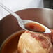 A Vollrath stainless steel basting spoon serving liquid over a piece of meat.