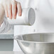 A chef using a Vollrath aluminum shaker to pour salt into a bowl.