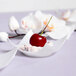 A cherry in a Fineline Tiny Tortes white plastic tray.