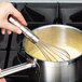A hand using a Vollrath stainless steel French whisk to stir white liquid in a pot.