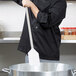 A man in a black chef uniform using a Carlisle Sparta paddle with a stainless steel handle to stir a large pot.
