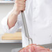 A chef holding a Vollrath hooked handle pot fork over a piece of ham.