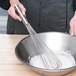 A person whisking a bowl of flour with a Vollrath stainless steel piano whip.