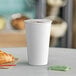 A white Choice paper hot cup filled with coffee sits on a table next to a croissant.