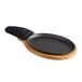 A black oval cast iron fajita skillet with a wooden underliner and handle cover.