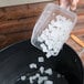 A person using a Baker's Mark clear plastic utility scoop to put ice in a container.