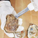 A person in gloves using a Dexter-Russell Sani-Safe oyster knife to open an oyster.