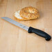 A Mercer Culinary Millennia 8" Bread Knife with a black handle next to a bagel.