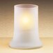 A Sterno frost glass candle holder with a lit white candle inside.