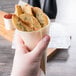 A hand holding a Tablecraft large wooden serving cone filled with potato wedges.