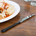 A plate of pasta with sauce and cheese and a WNA Comet Reflections Duet stainless steel look plastic knife.
